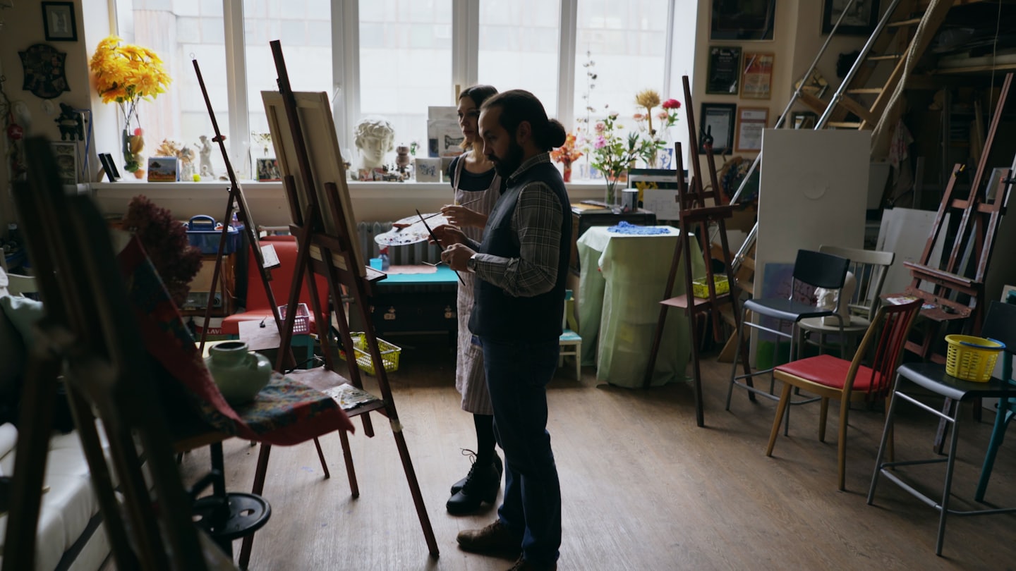 Artists collaborate in a sunlit art studio with supplies.